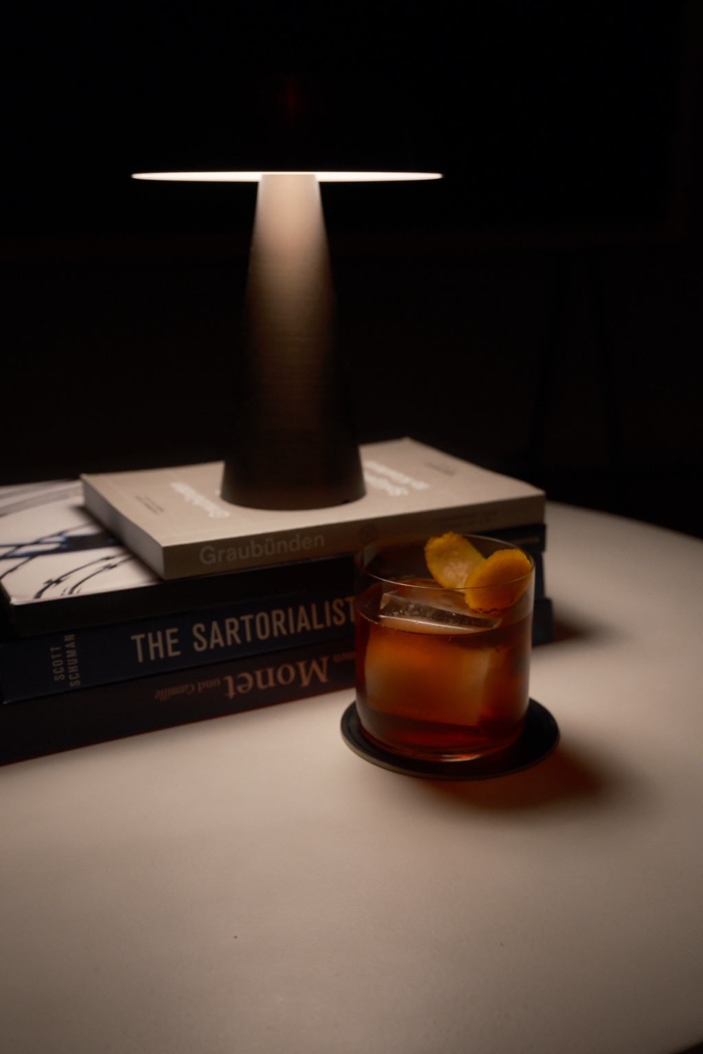 Marvin’s homemade Negroni with orange peel beside a stack of books and a glowing table lamp